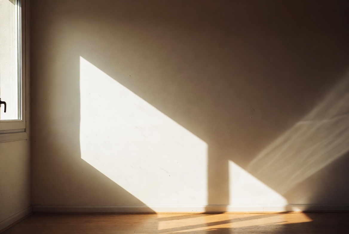 Soft light entering through a window, casting clean rectangular patterns on the wall and floor of a quiet room.